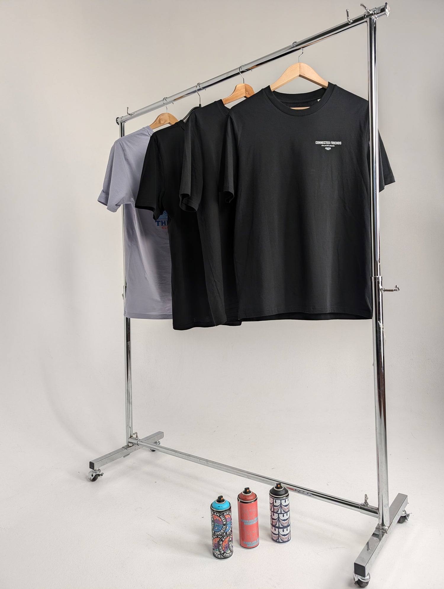 Auswahl der Bio Baumwoll T-Shirt Kollektion von DreieckDreieck an einer Kleiderstange präsentiert, mit Sprühdosen als urbanes Stilelement.